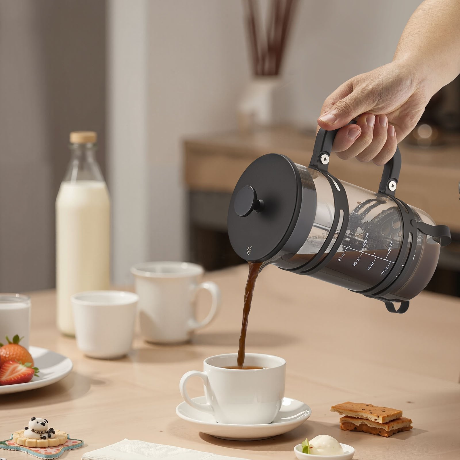 Person pouring coffee from a French press into a white mug on a wooden table.